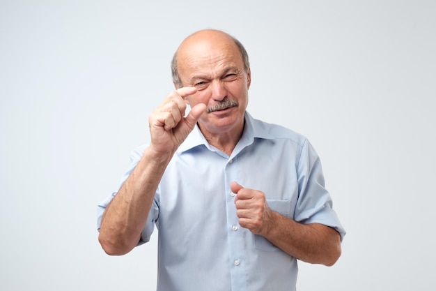 Senior man met snor die iets kleins laat zien met vijgen Hij is boos op zijn financiën