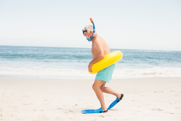 Senior man met zwemmen ring en flippers op het strand