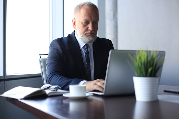 Photo senior man in office working on laptop computer in modern office.