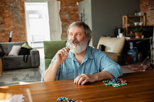 Senior man playing cards and drinking wine with friends looks happy