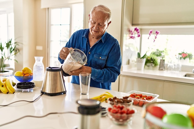 Senior man pouring smoothie on glass at kitchen