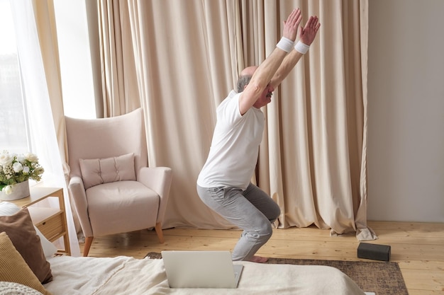 写真 椅子のポーズ utkatasana を行う自宅でヨガを練習している年配の男性