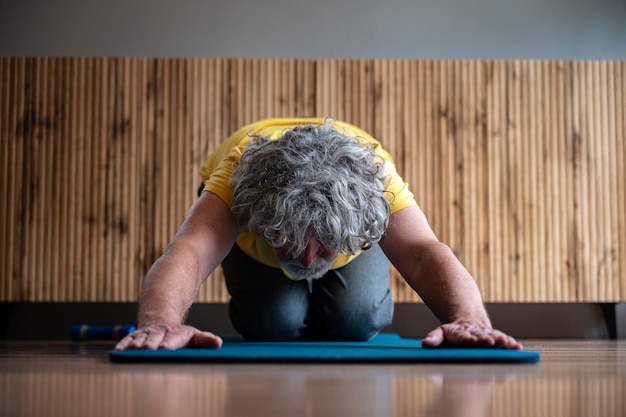 Foto uomo anziano che pratica yoga o pilates facendo la postura di un bambino