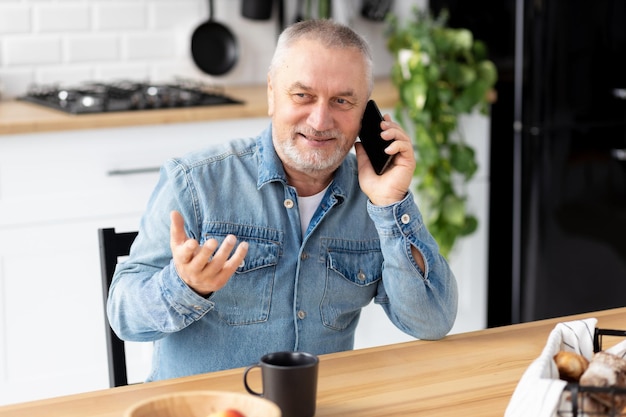 Senior man praten aan de telefoon zittend aan de tafel in de keuken thuis