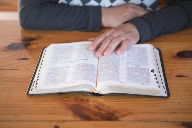 Senior man praying, reading an old Bible. Hands folded in prayer on a Holy Bible in church concept for faith, spirituality and religion