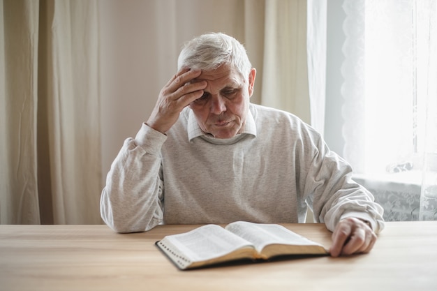 Senior man praying, reading  an old Bible in his hands.