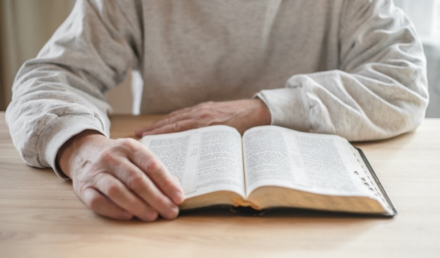 Senior man praying, reading  an old Bible in his hands.