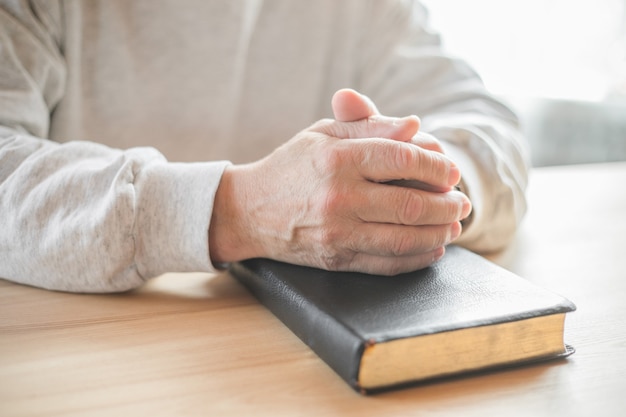 Senior man praying, reading  an old Bible in his hands.