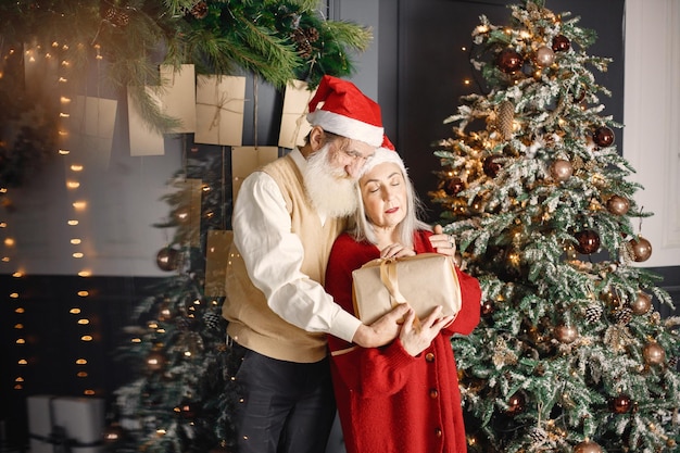 Senior man presenteert kerstcadeau aan zijn vrouw die bij de kerstboom staat