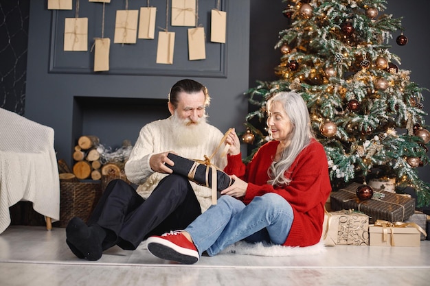 Senior man presenteert kerstcadeau aan zijn vrouw die bij de kerstboom zit