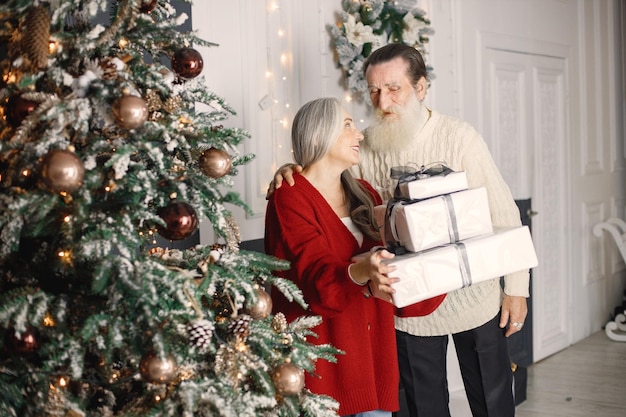 Senior man presenting christmas gift to his wife standing near\
christmas tree