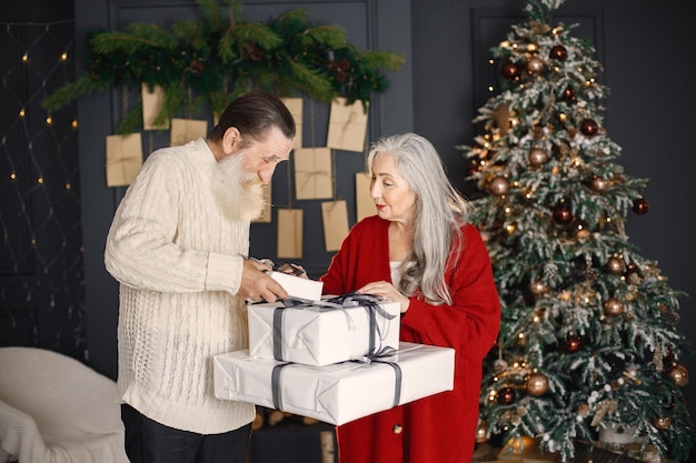 Senior man presenting christmas gift to his wife standing near christmas tree