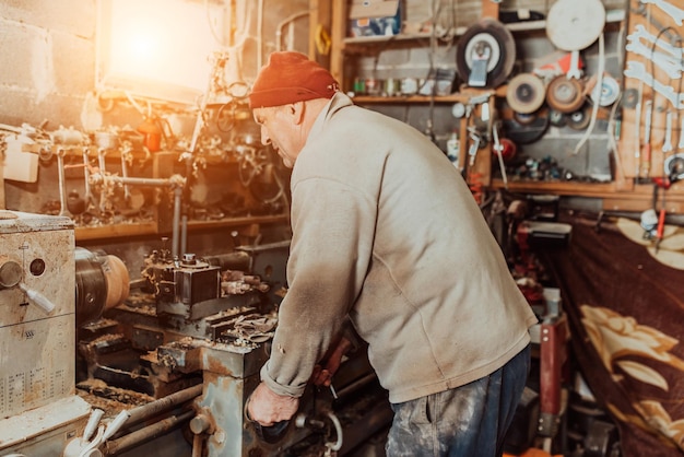 A senior man procesing wood on a lathe and making wooden dishes in the workshop.