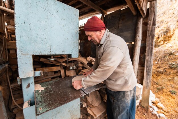 屋外の作業場で機械で木材を加工する年配の男性