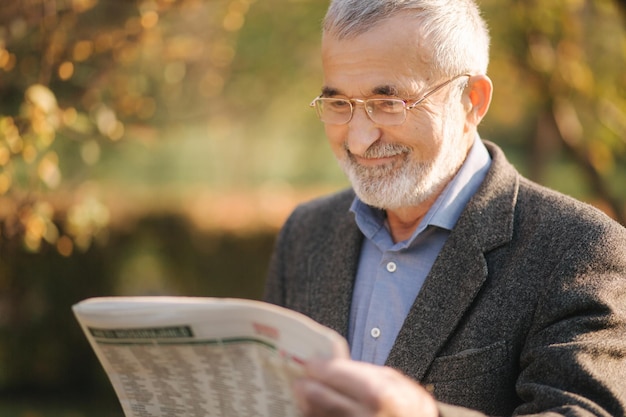 Photo senior man read a newspaper in the park background of yellow tree in autumn