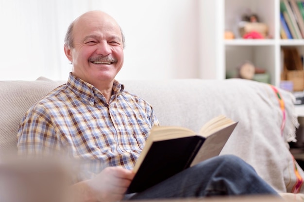 Старший мужчина читает книгу на диване