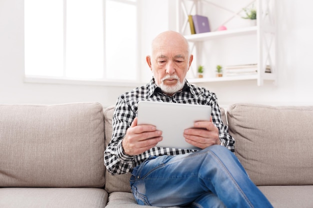 Senior man reading news on digital tablet. Relaxed mature male using portable computer at home, copy space