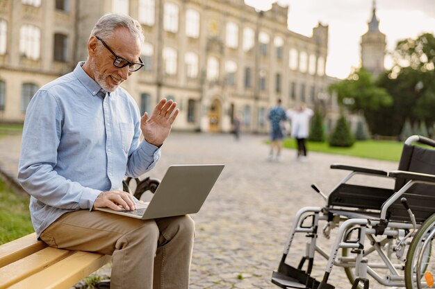 Senior man recovering patient with wheelchair having video call working on a laptop while sitting