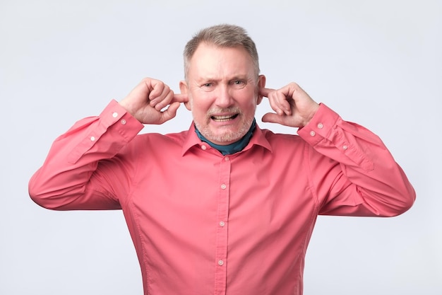 Photo senior man in red shirt plugging ears with fingers