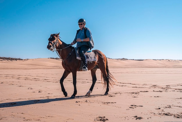 Senior man rijdt paard langs de kustlijn op het strand tegen heldere hemel