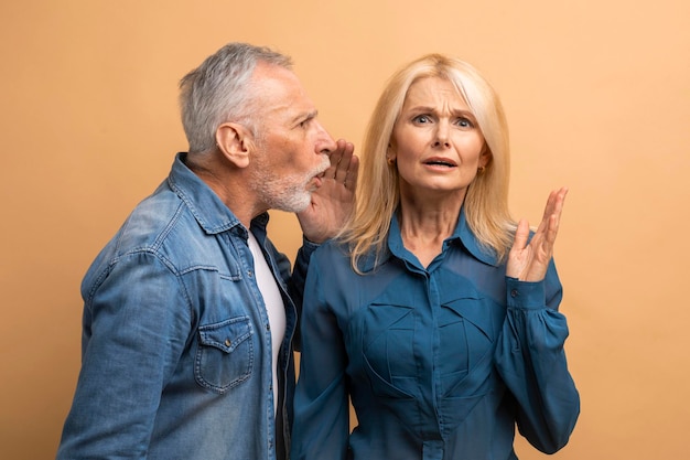 Photo senior man sharing secret with his wife beige background