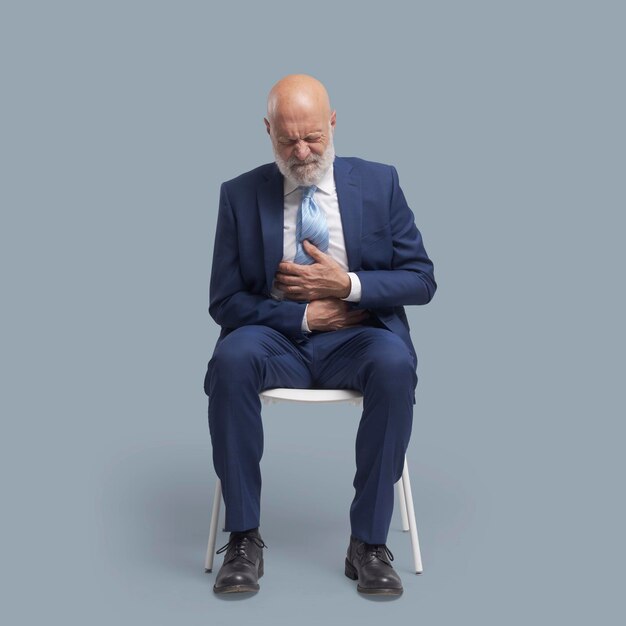 Photo senior man sitting on a chair and having a bad stomach ache