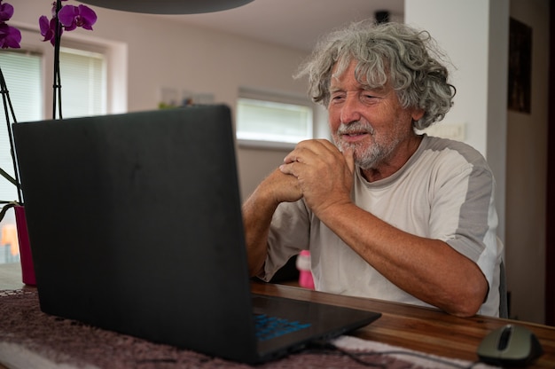 Photo senior man sitting at his dining table with a laptop computer in front of him