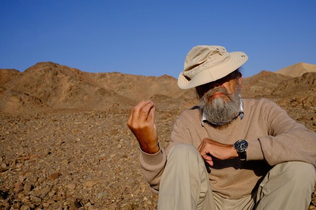 Senior man sitting on mountain against clear sky