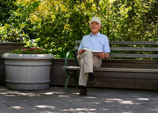 Фото Старший мужчина сидит на скамейке на улице и читает книгу