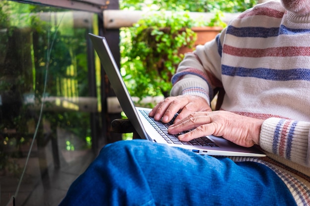 Foto senior uomo seduto all'aperto in balcone in legno durante l'utilizzo del computer portatile. anziani caucasici che si rilassano all'aperto in un rustico chalet di montagna