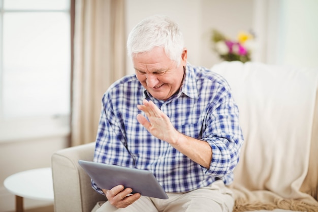 Senior man sitting on sofa and using digital tablet in living room