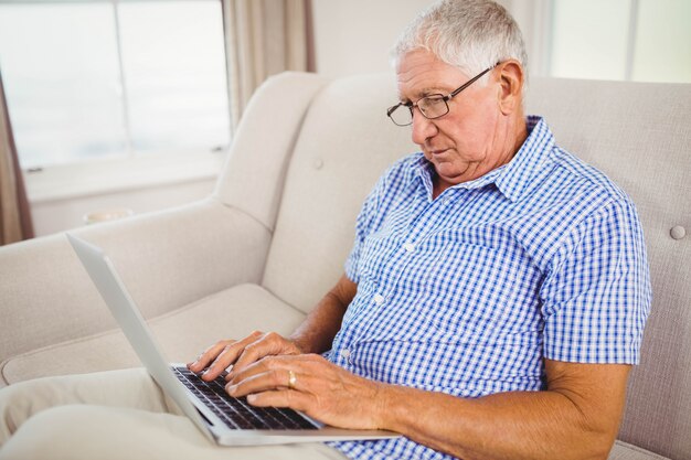 Senior man sitting on sofa and using laptop in living room