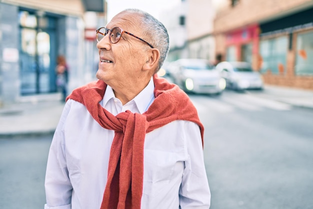 Senior man smiling happy wearing glasses walking at the city.