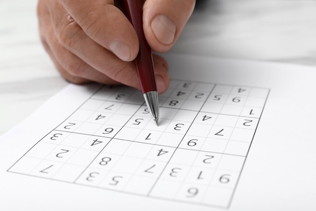 Foto uomo anziano che risolve puzzle di sudoku al primo piano tavolo bianco