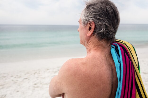 Senior man standing on beach with towel on shoulder