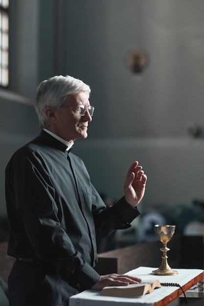 Senior man standing with the Bible in front of the altar and praying