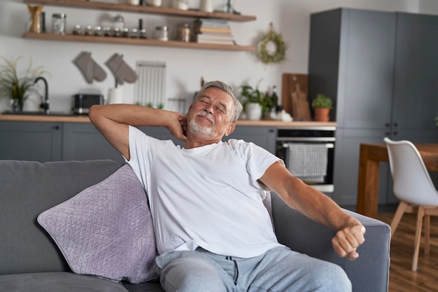 Senior man stretching at morning and sitting at couch