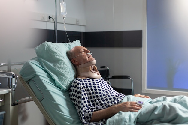 Старший мужчина страдает после серьезной аварии, лежа на больничной койке