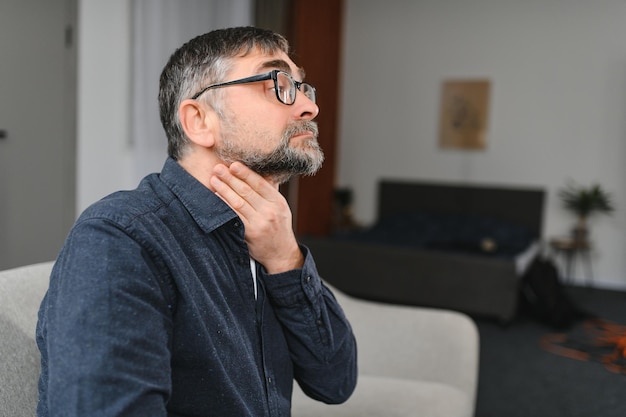 Foto uomo anziano che soffre di raffreddore foto di un uomo anziano che ha mal di gola uomo caucasico anziano che si tocca la gola mal di gola tonsillite o problema alla ghiandola tiroidea uomo anziano a casa che non si sente bene