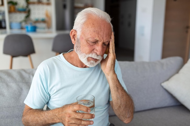 Senior man suffering from a headache at home Worried senior man sitting alone in his home This headache really hurts My head is killing me