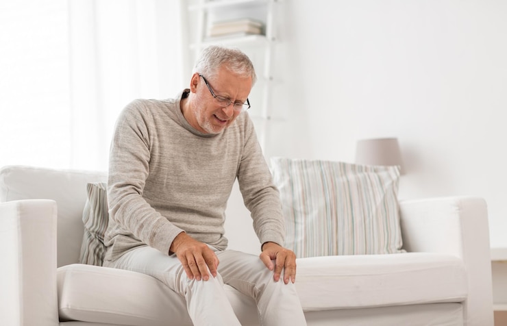 Photo senior man suffering from knee ache at home
