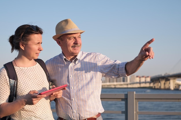 Senior man in summer hat shows the way on the map to young woman