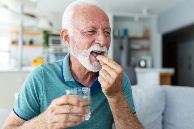 Старший мужчина принимает таблетку со стаканом воды в руке Зрелый мужчина в стрессе пьет успокоительные антидепрессанты Мужчина чувствует себя подавленным, принимая наркотики Лекарства на работе
