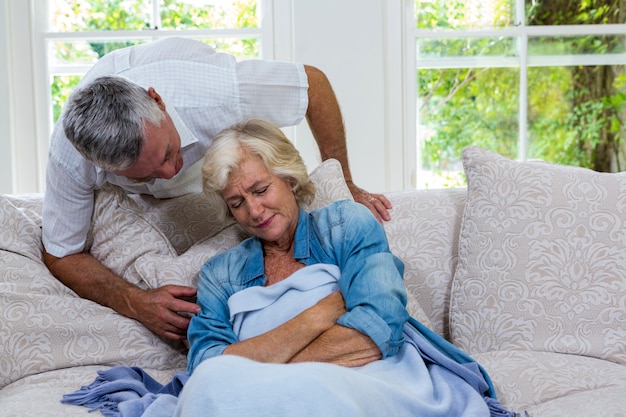 Senior man talking to ill wife resting on sofa