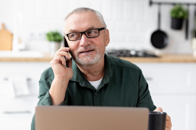 Uomo anziano che parla al telefono con il laptop