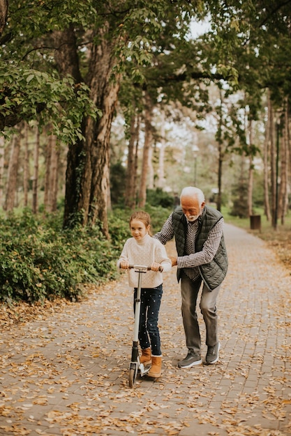 Старший мужчина учит внучку кататься на самокате в парке