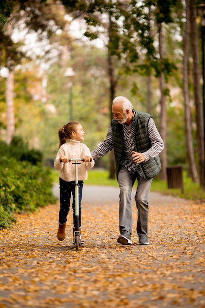 Senior man teaching his granddaughter how to ride kick scooter in park