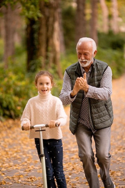 Senior man teaching his granddaughter how to ride kick scooter in park