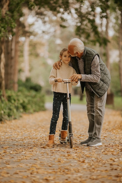 Senior man teaching his granddaughter how to ride kick scooter in park