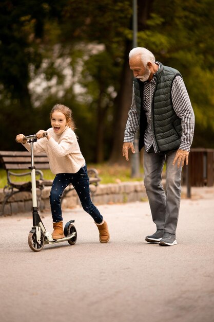 Senior man teaching his granddaughter how to ride kick scooter in park